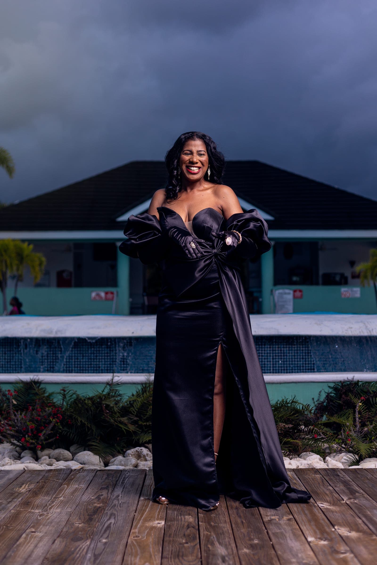 Woman in a black off-shoulder gown on a wooden deck under a stormy evening sky